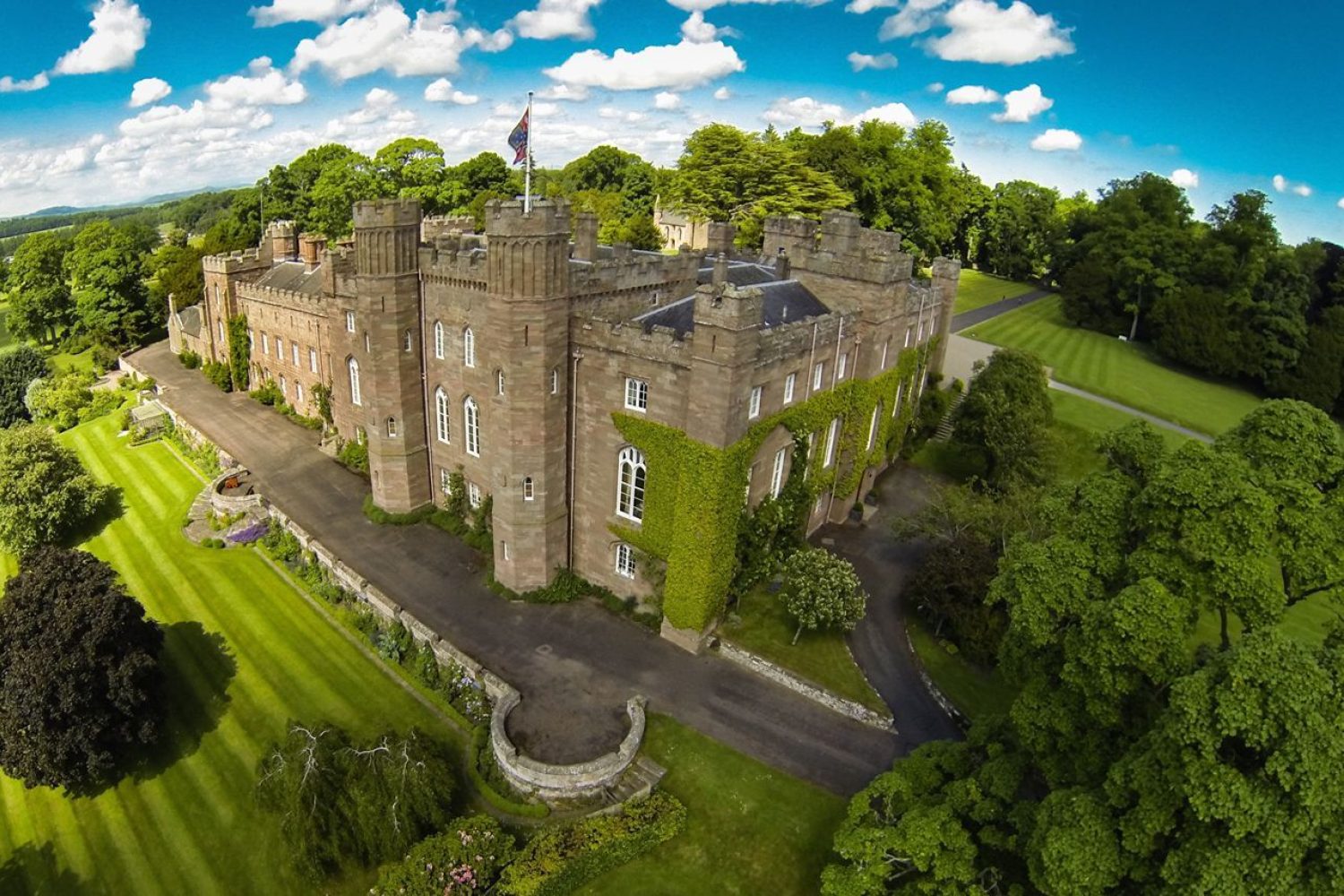 Large Scottish palace and its grounds with blue skies, green lawns and trees