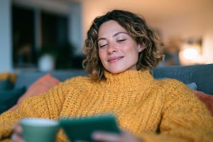 A young woman in a yellow jumper reading an e-book with a cup of tea in a green mug