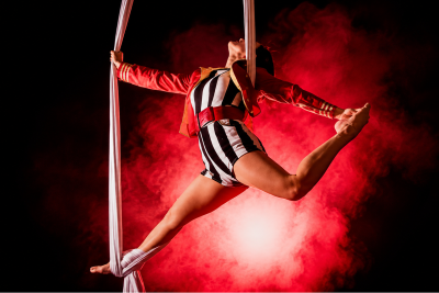Striped black and white costume on woman on pink circus silks with red light behind her