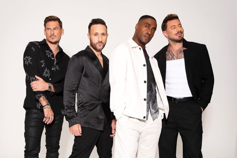 Band image of Blue. Four men wearing black and white on a white background.