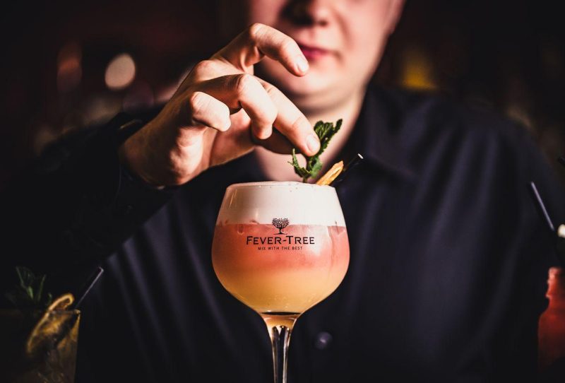 a hand placing a green sprig into an orange cocktail
