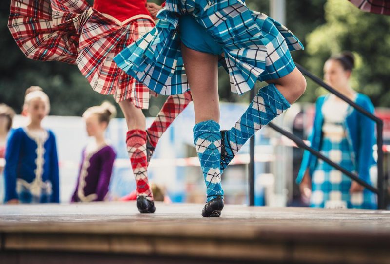 two sets of women's legs dancing the highland fling, one in red socks and one in blue socks