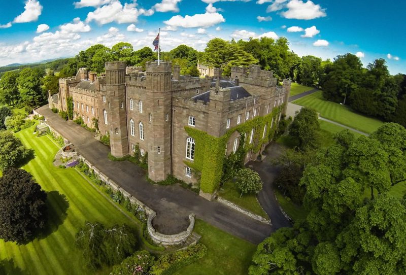 Large Scottish palace and its grounds with blue skies, green lawns and trees