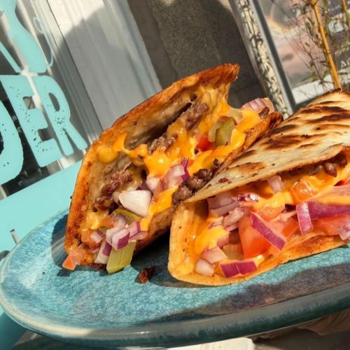 Smash burger tacos with lettuce, gherkins, onion, tomato, cheddar and burger sauce on a blue plate