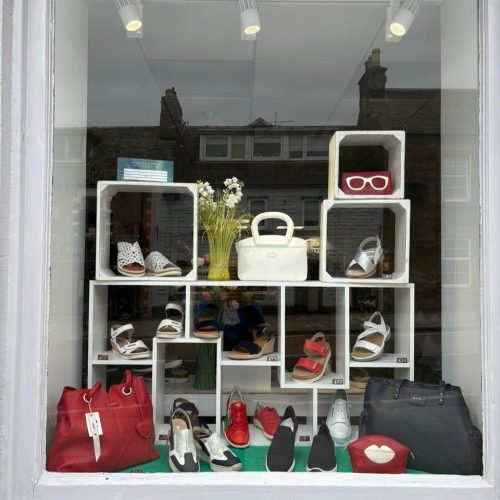 Window display with colourful shoes, bags  on a white large shelving unit.