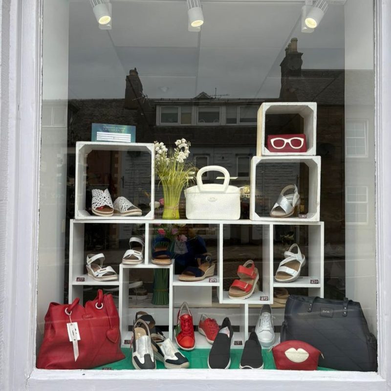 Window display with colourful shoes, bags  on a white large shelving unit.