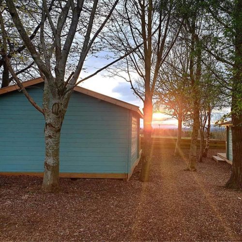 Turquoise painted cabin  surrounded by trees with a sunset in background