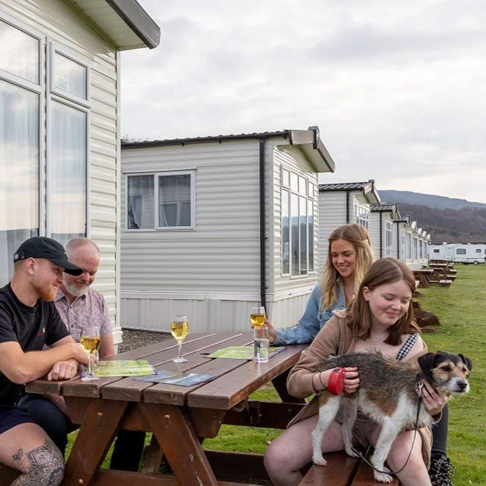 Smiling family and dog ,sitting at a table with caravans in the background