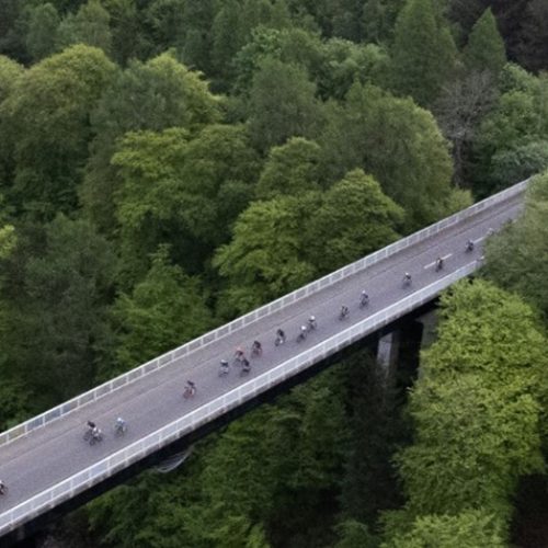 Grey concrete bridge over river in Pitlochry surrounded by various green shades of trees.
