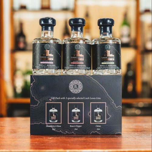 Three small bottles of gin sitting on a table on top of their packaging.