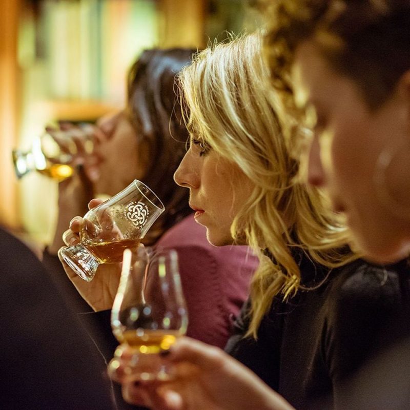 Three women in a line, drinking an amber liquid at Dewars Aberfeldy Distillery