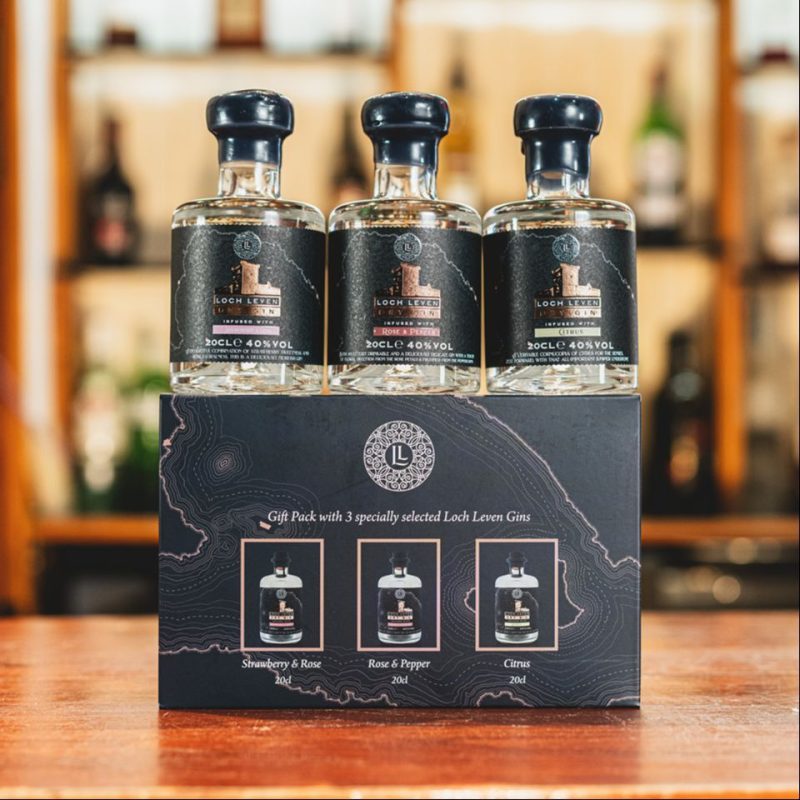 Three small bottles of gin sitting on a table on top of their packaging.