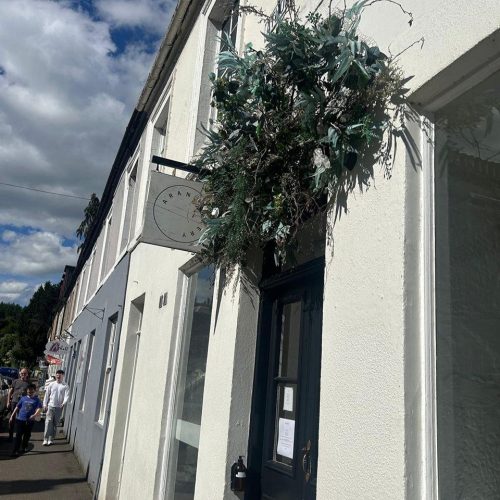 Sign outside shop for Aran Bakery with a decorative flower wreath above door.