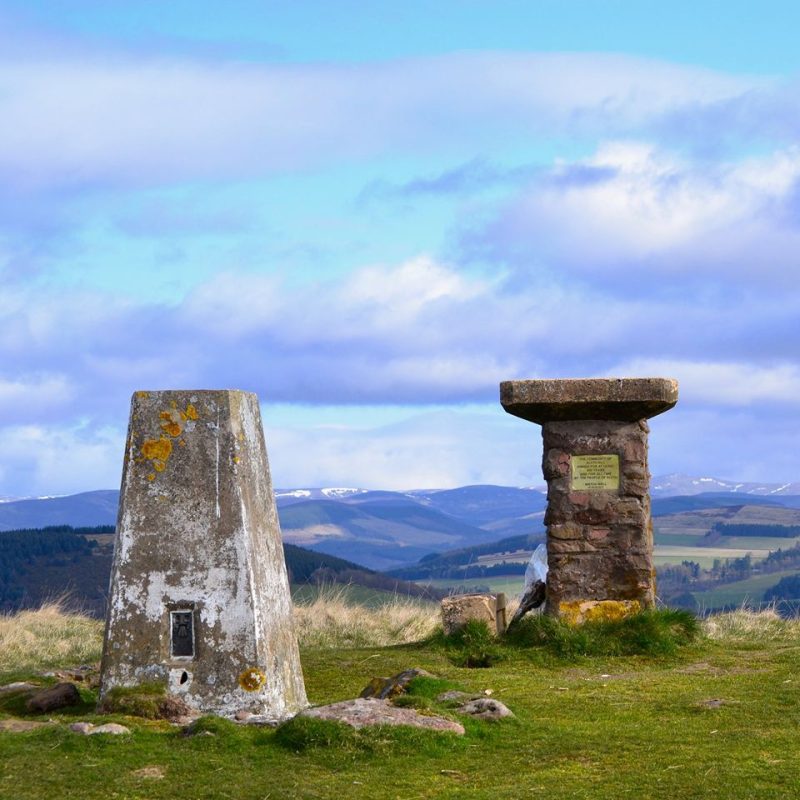Two stone markers, green grass with green hills with cloudy blue skies.