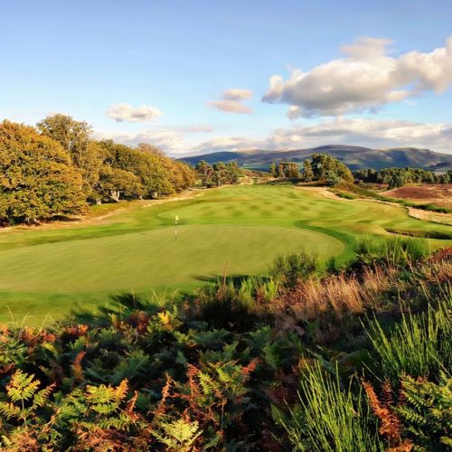 Long green fairway with lush green trees on left side and mountains in the distance at Gleneagles, Scotland.