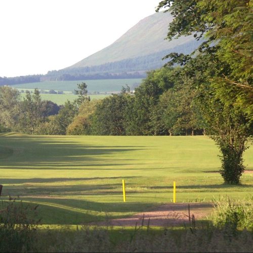Green fairway with sand bunker and green trees and hills in the distance.
