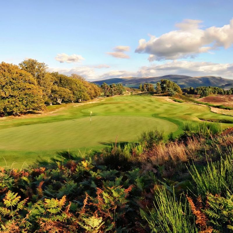 Long green fairway with lush green trees on left side and mountains in the distance at Gleneagles, Scotland.