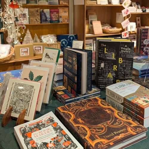 Book displayed on a table alongside cards, and shelving units behind filled with books.