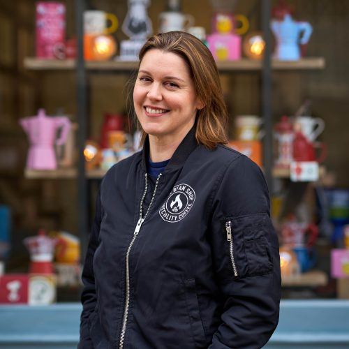 Smiling lady in front of a shop window with coffee and tea accessories.