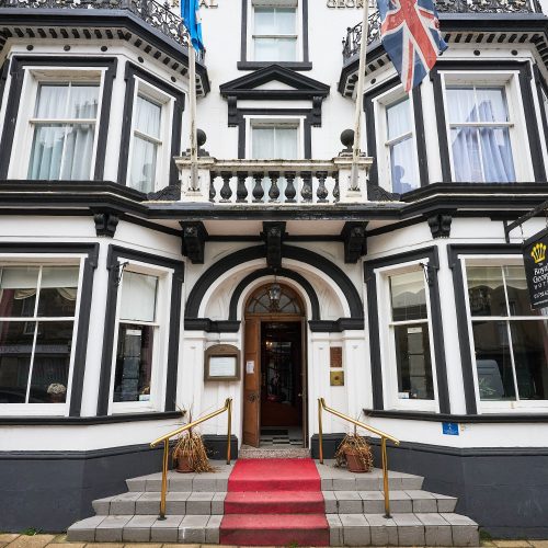 Large Victorian Hotel. painted white with black trim around doors and windows with steps and a red carpet.
