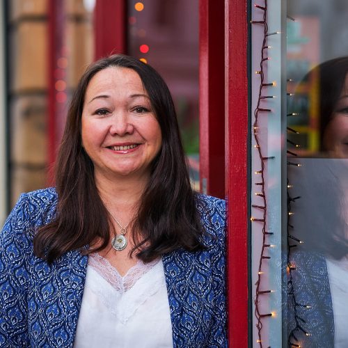 Smiling dark haired woman outside a red shop front