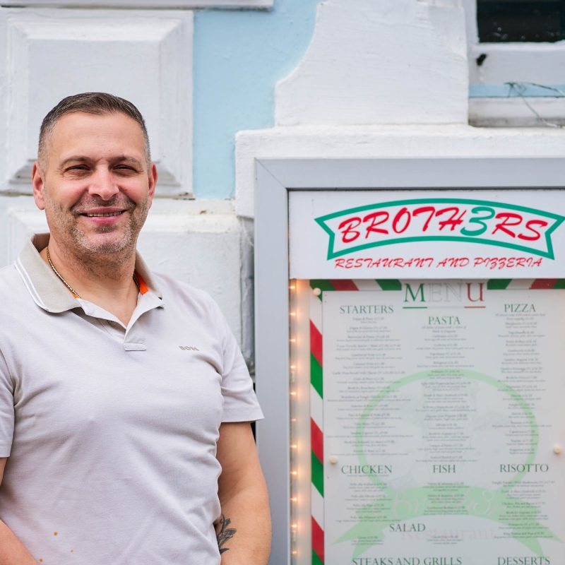 Smiling man in front of Menu board for Broth3rs Restaurant