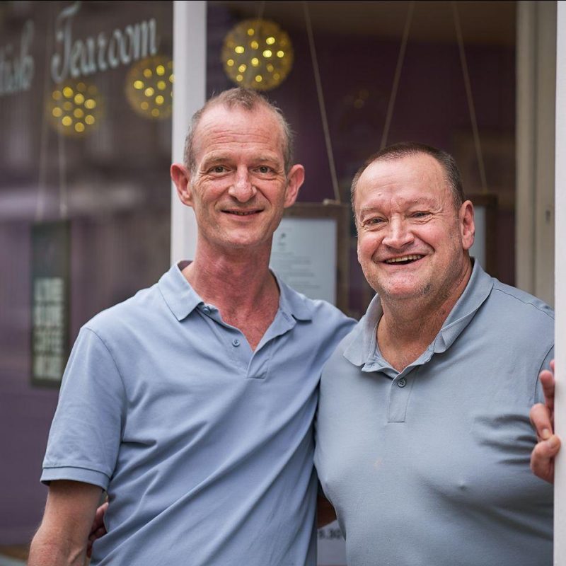 Two smiling men in grey shirts in  a doorway to George Street Tea room