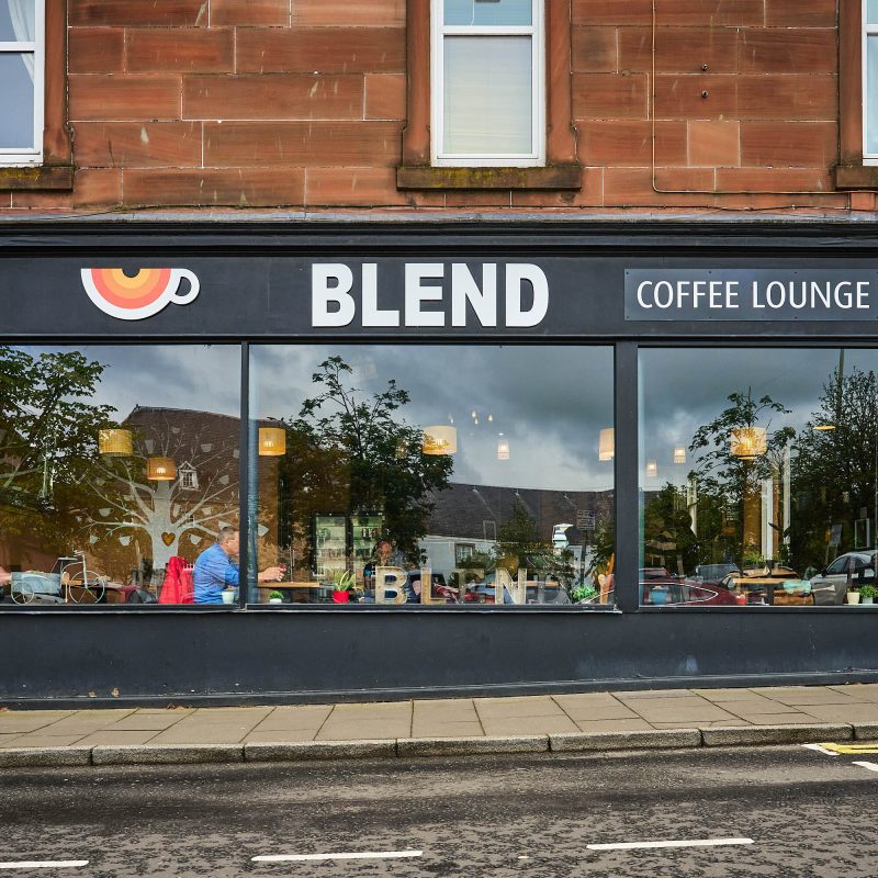 A black building with white text painted on it saying 'Blend'. On the left of the text is a orange and white coffee cup which is Blends logo