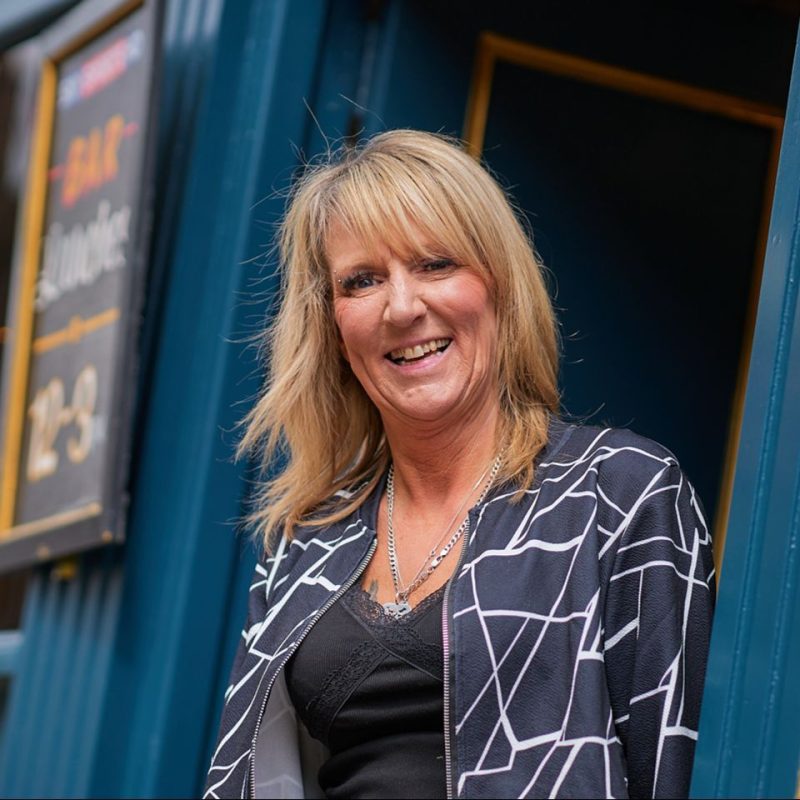 Smiling blonde haired woman in a teal painted doorway, Ormand Bar, Perth, Scotland