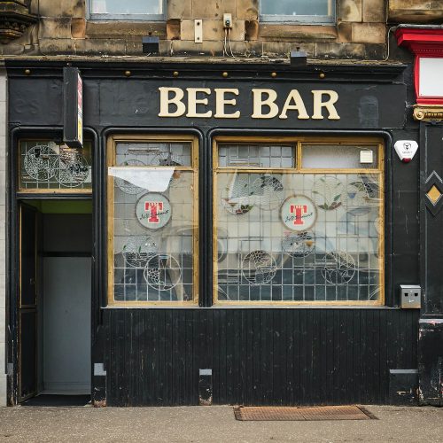 An black building with gold accents around the window. There is a gold sign which says 'Bee Bar'.