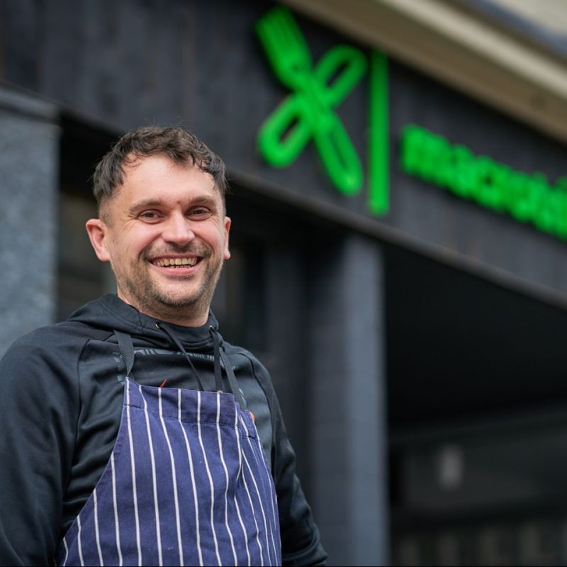 Smiling man with blue and white apron stands below a shop sign for Macrotrition in Perth, Scotland