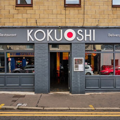 Grey painted shop front with Koku Shi in white letters, white circle with red circle inside between Koku and Shi.