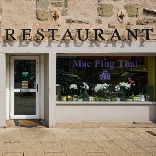 A brick building with white accents, on the window in purple letters it says 'Mae Ping Thai'