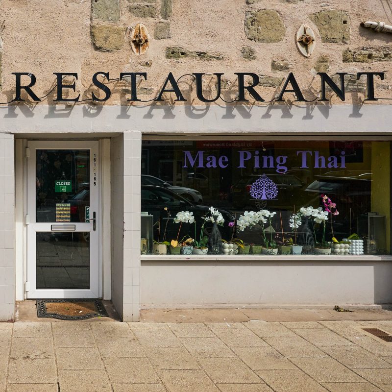 A brick building with white accents, on the window in purple letters it says 'Mae Ping Thai'