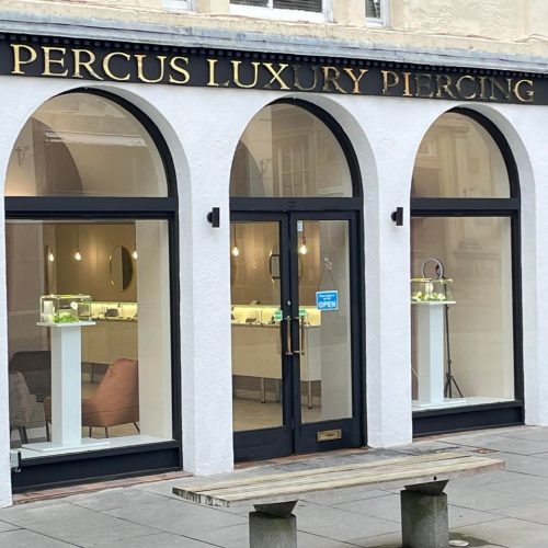 Three windows with arches at top and black and gold sign above for Percus Luxury Piercing