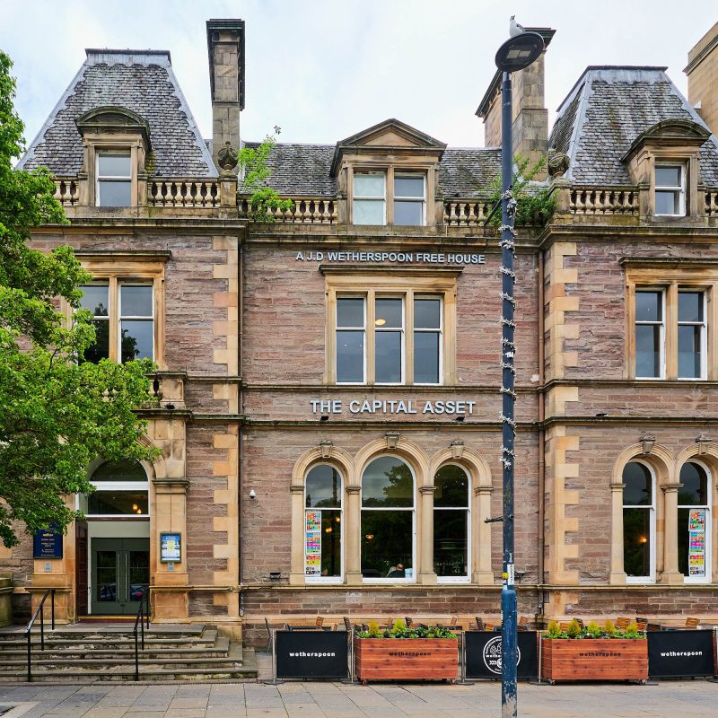 A large two storey brick building with large windows and and outside seating area with two arched stone doorways on either side