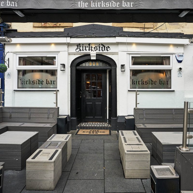 A white building with a black doorway, It has some dark grey outdoor seating.