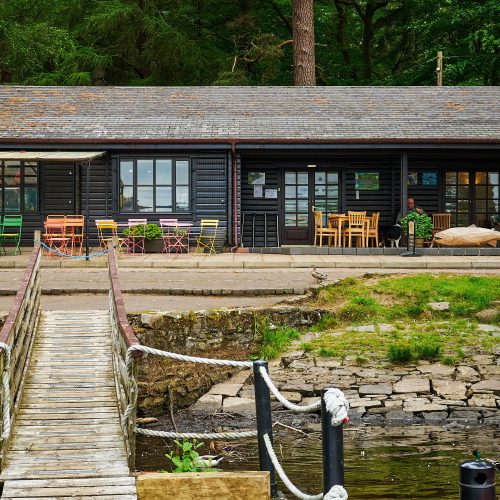 A black building with a small body of water in front of it and a wooden bridge.