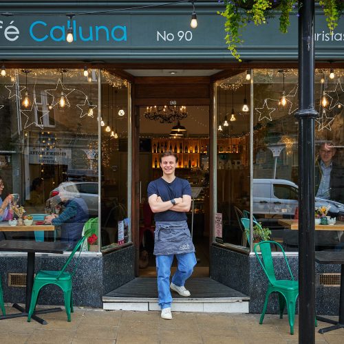 A smiling man wearing a apron with the logo for Cafe Calluna embroidered on it.