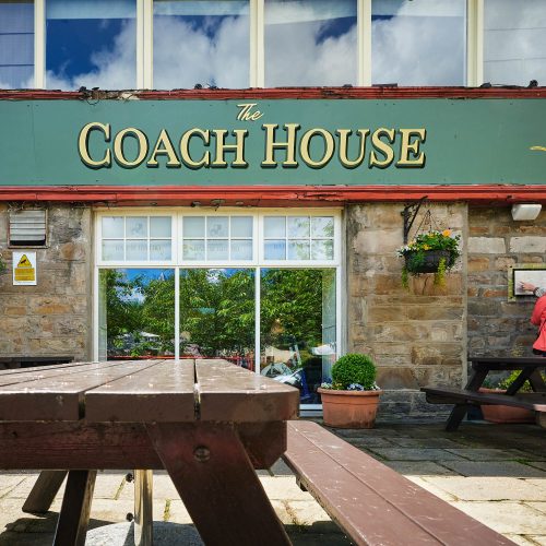 A brick building with a green sign which reads 'The Coach House.'
