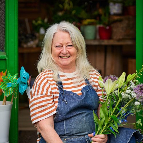 A smiling woman holding a green and purple bouquet of flowers.