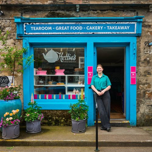 A smiling woman standing in front of a blue cafe.