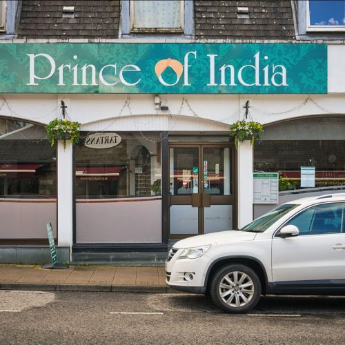 White painted building with signage for Prince of India, white car in foreground