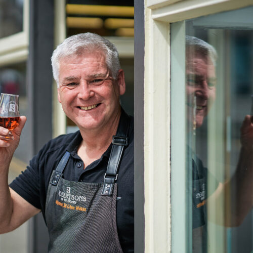 A smiling man holding a glass of whiskey.