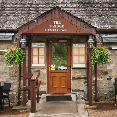 A brick building with brown accents and a sign which reads 'The Bridge Restaurant'
