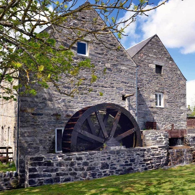 Two old stone building with large woode33n watermill and a stone wall under a blue sky, Blair Atholl watermill