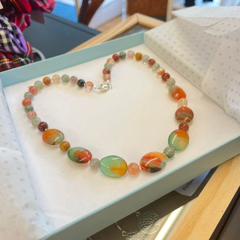 Coloured gemstone necklace in a padded blue box on a table.