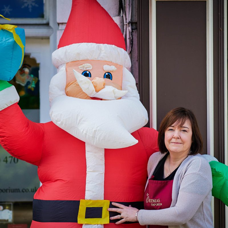 A smiling woman standing next to a giant inflatable Santa Clause.
