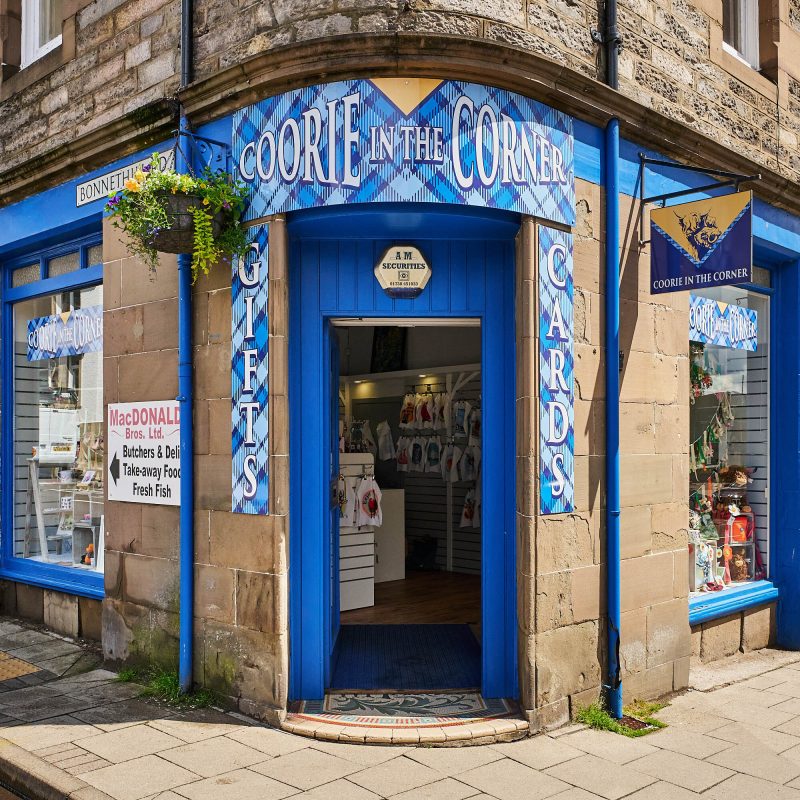 A brick building with a blue tartan sign which reads 'Coorie in the Corner'.