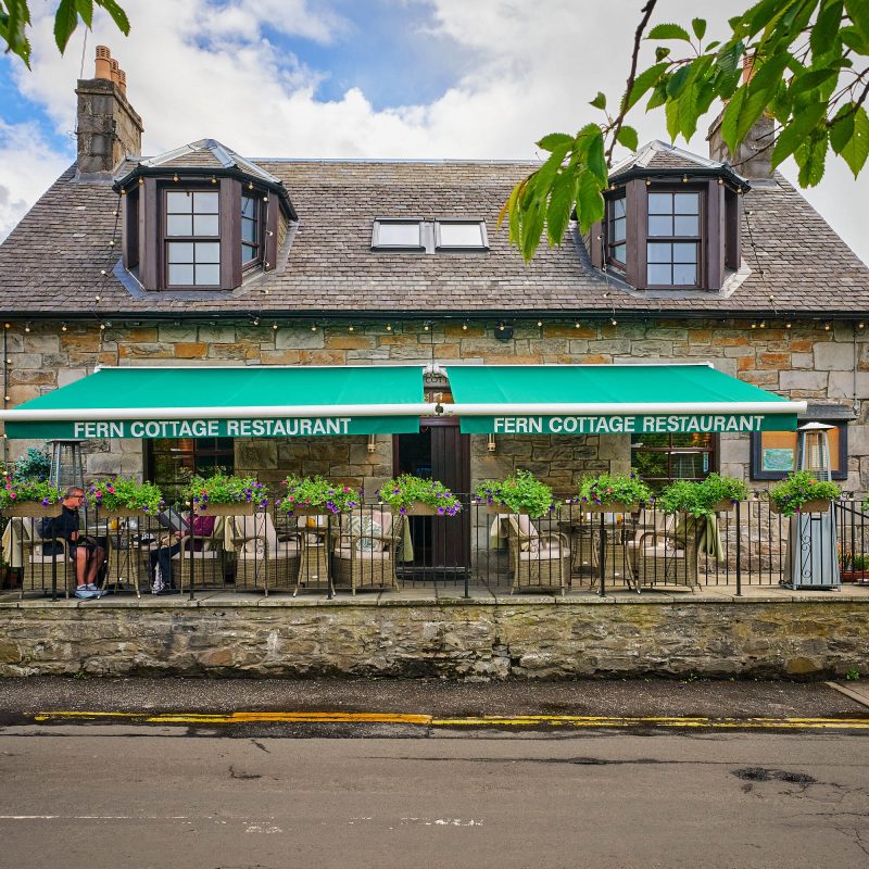 A brick cottage with a green sign which reads 'Fern Cottage Restaurant.'